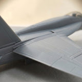 Gray plastic aircraft model kit shown close up, highlighting molded wing and fuselage panel lines against a blurred beige background.