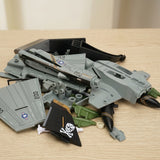 Gray plastic aircraft model kit parts lie on a light wooden tabletop, including black pirate-marked tail fins and green accessories.
