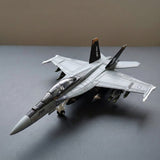 Assembled gray plastic aircraft model kit sits diagonally on a gray surface with a clear canopy, extended landing gear, and black tail fins.