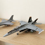 Assembled gray plastic aircraft model kit with pirate-marked tail fins rests on a wooden shelf beside another partially visible gray aircraft.
