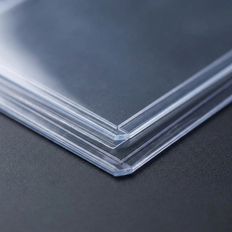 Clear PVC card sleeves are stacked on a dark gray textured surface, with their layered edges and corners shown close up.