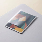 A clear card sleeve partially covers a colorful geometric card resting on a light gray textured surface.