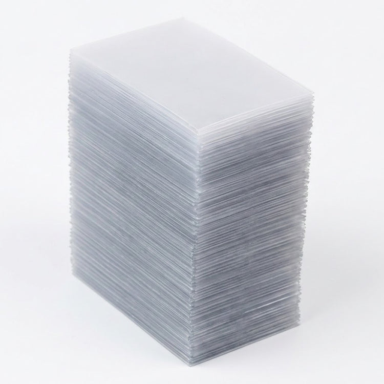 A tall rectangular stack of empty clear card sleeves viewed at an angle against a white background.