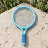 A light blue plastic racket from the toy racket set rests on beige stone, with white mesh and a darker blue grip.