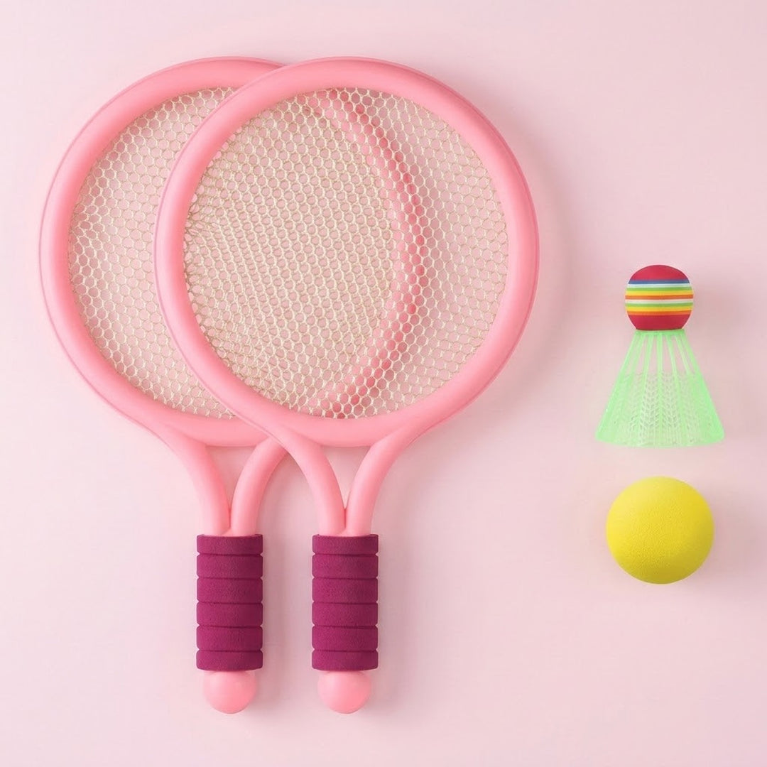 Pink plastic toy racket set with purple grips, white mesh, a yellow ball and green shuttlecock on a pale pink background.
