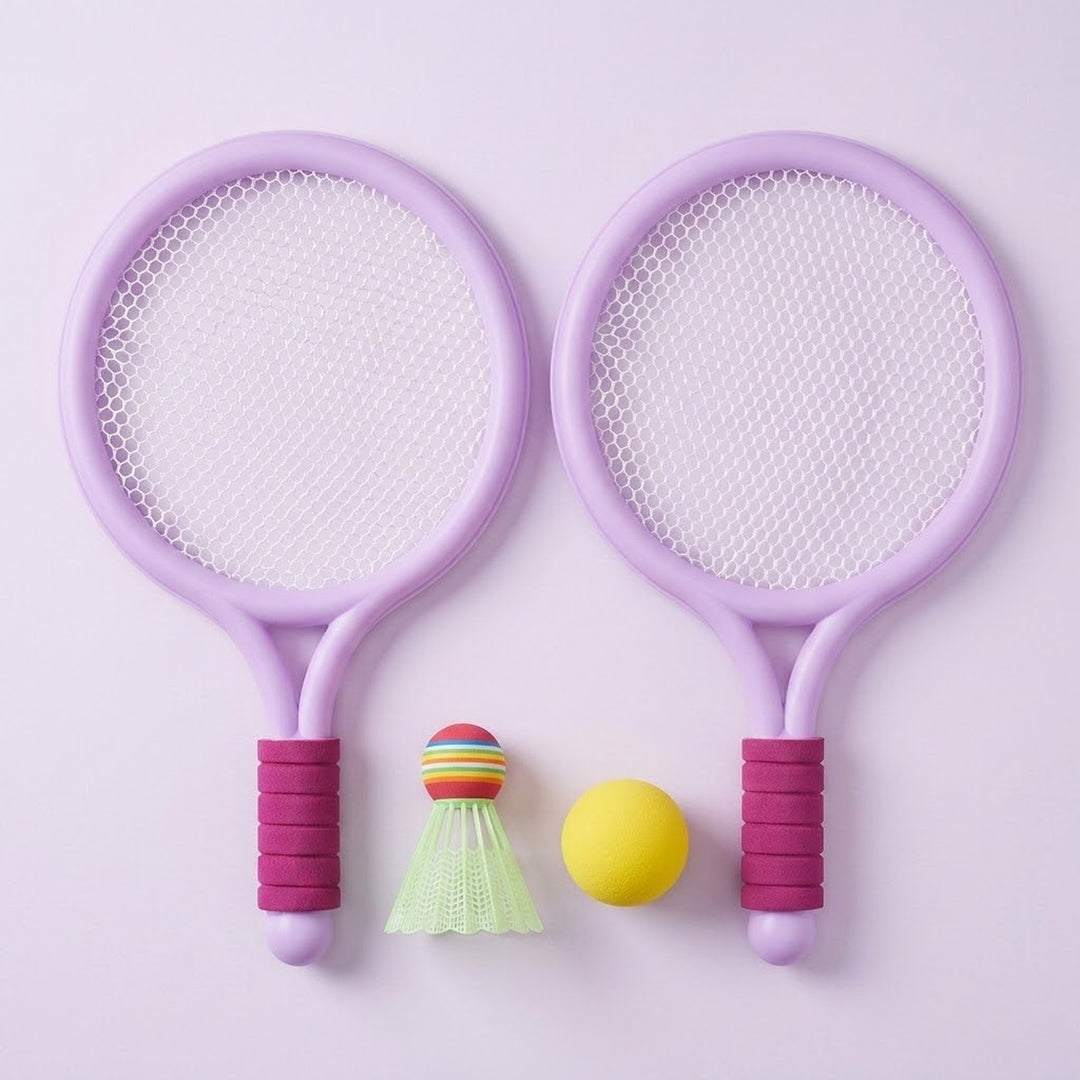 Light purple plastic toy racket set with pink grips, white mesh, a yellow ball and green shuttlecock on a pale lavender background.