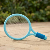 Blue plastic toy racket with white mesh and a ribbed blue grip rests at an angle on sunlit outdoor paving.