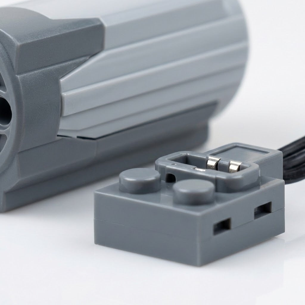 Gray building block accessory cable connector with exposed metal contacts sits beside a ribbed motor housing on a white surface.