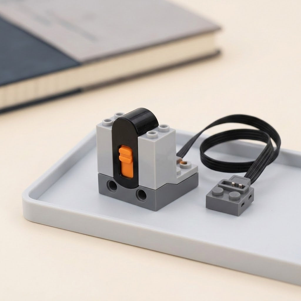 Gray and black building block accessory receiver with an orange switch and looped black cable rests on a gray tray beside notebooks.