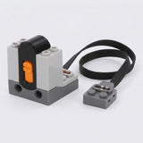 A LEGO-compatible electrical relay module with a black and gray plastic body, an orange switch, and a black wire connector, shown on a light gray background.