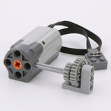 Gray building block accessory motor with an orange axle opening, black cable, and two interlocking gray gears rests on a white background.