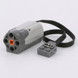 A LEGO-compatible motor module with a gray and white body, an orange center pin, a black cable, and a small gray connector piece on a white background.
