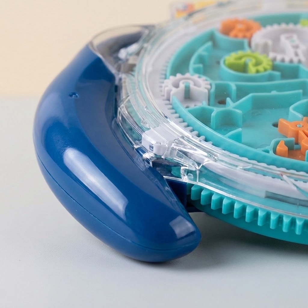 Close-up of a maze puzzle showing a curved blue handle, transparent cover, turquoise tracks and colorful gears against a pale background.