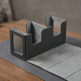 A black-and-gray deck box sits open on a wooden tabletop with its folding cover laid flat, revealing compartments and display windows.