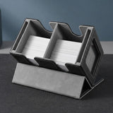 Black deck box with gray lining holds two card stacks, tilted on its folded cover on a dark tabletop.