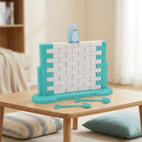 A turquoise and white plastic balance game with a blue penguin and two tools sits on a wooden table beside floor cushions.