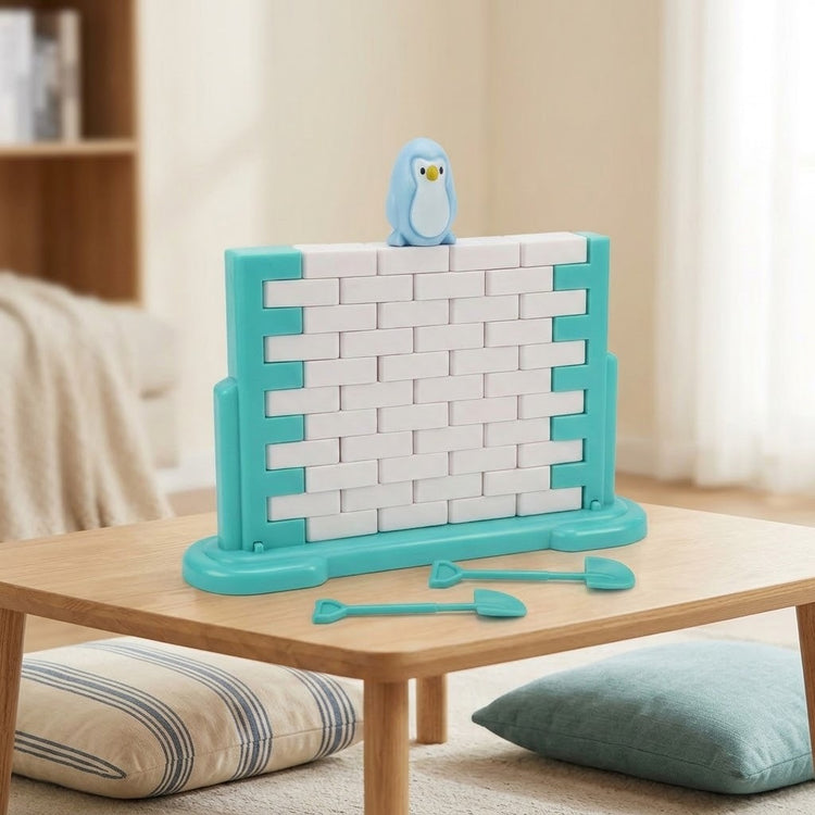 A turquoise and white plastic balance game with a blue penguin and two tools sits on a wooden table beside floor cushions.