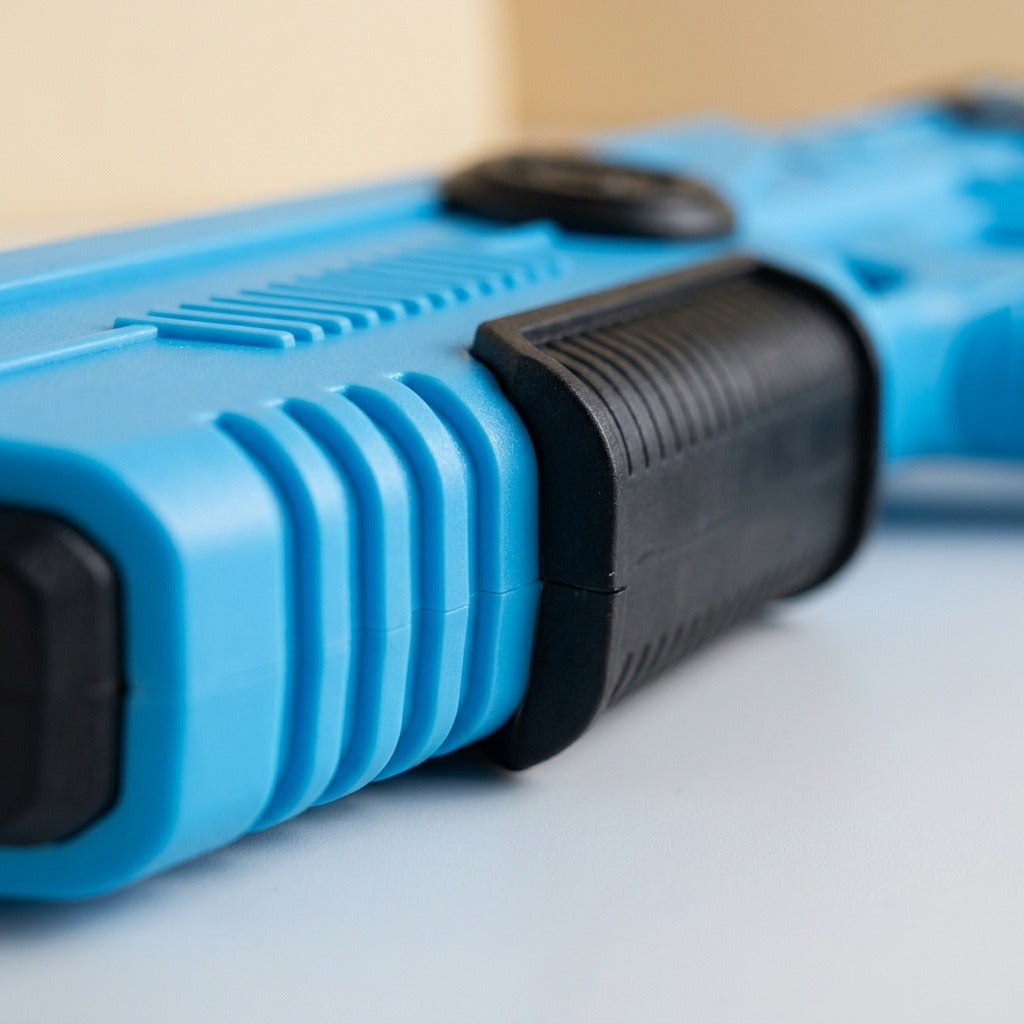 Close-up of a blue and black water gun shows ridged detailing on a light surface against a beige background.