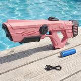 A pink and black toy water gun is displayed on a wooden deck with a swimming pool in the background, alongside a blue battery and a black USB charging cable.