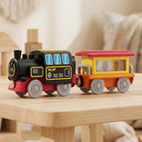 A wooden toy train set with a black locomotive and a yellow, orange, and red passenger car, displayed on a light wooden table in a softly blurred indoor setting.