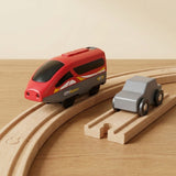 A toy train set on wooden tracks, featuring a red and gray toy high-speed train with yellow accents and a gray toy car, photographed on a light wood tabletop against a warm beige background.