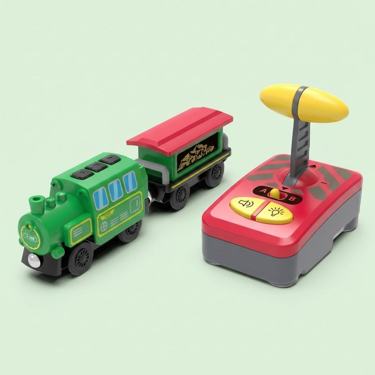 A toy train set with a green and red train engine pulling a matching cargo car, shown next to a red and gray remote control with a yellow antenna on a pale green background.