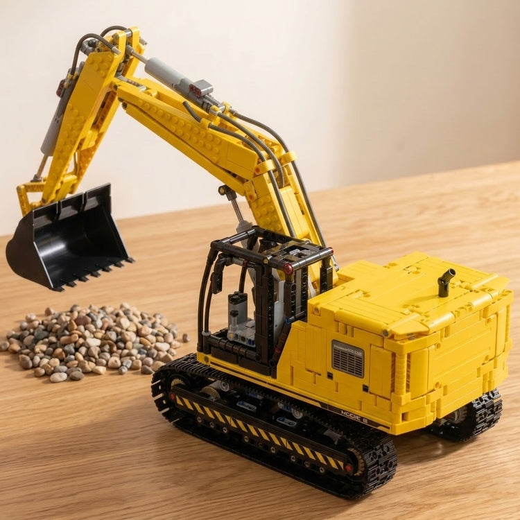 Yellow and black plastic excavator building set assembled with a raised bucket on a wooden tabletop beside a pile of pebbles.