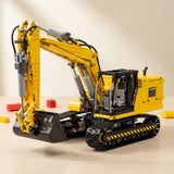 A yellow and black building block excavator toy with a front attachment, photographed on a light wood surface against a soft beige background.