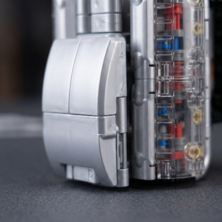 V8 engine model kit close-up showing silver plastic housing and a transparent side panel revealing red and blue components against dark surroundings.