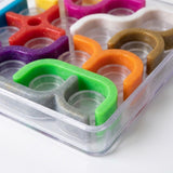 Mechanical puzzle close-up showing colorful curved plastic pieces, glittery surfaces, circular recesses, and the clear tray rim against a white background.