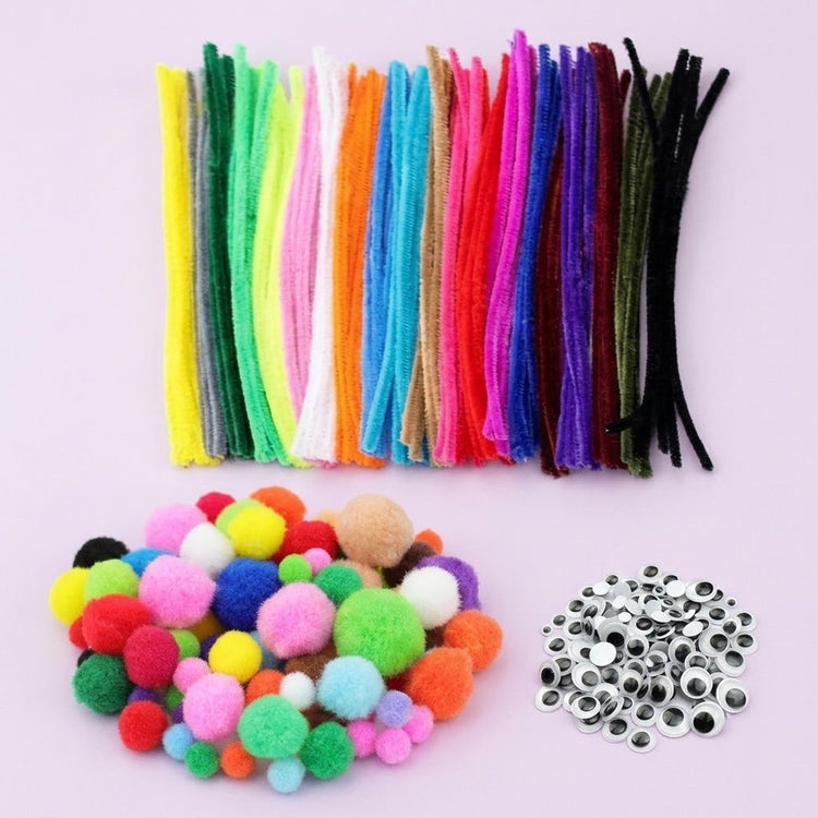 A craft kit with colorful pipe cleaners, multicolor pom-poms, and silver eye stickers arranged on a light pink background.