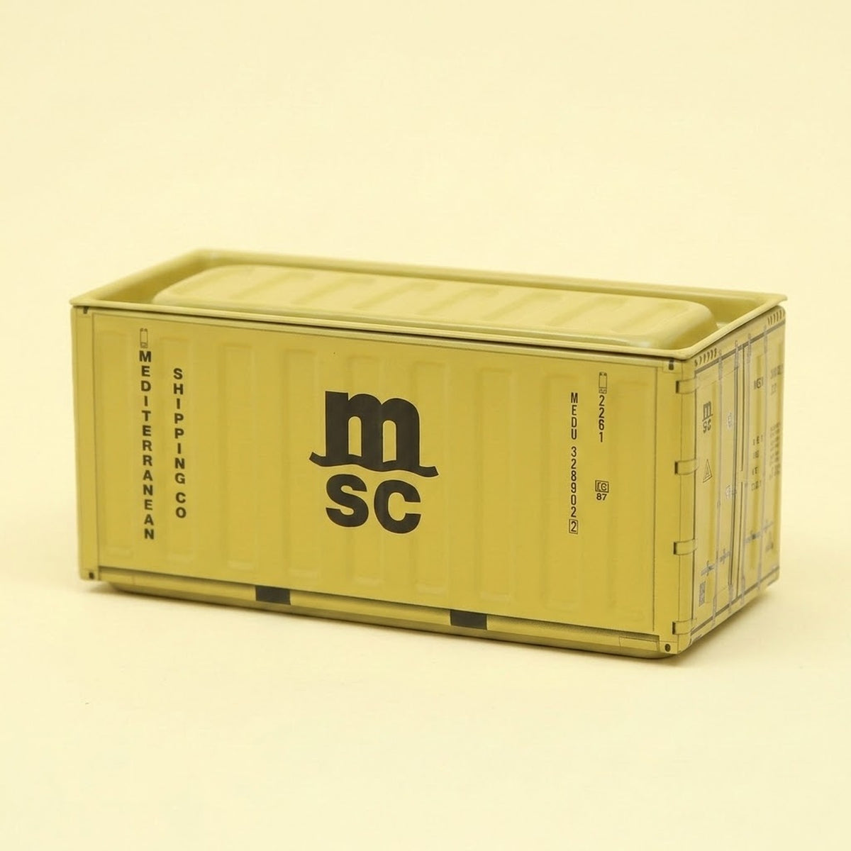 A mustard-yellow metal storage box with black lettering, ribbed sides, and a closed lid sits against a pale cream background.