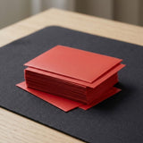 Red matte polypropylene card sleeves stacked on a black playmat on a light wooden desk.