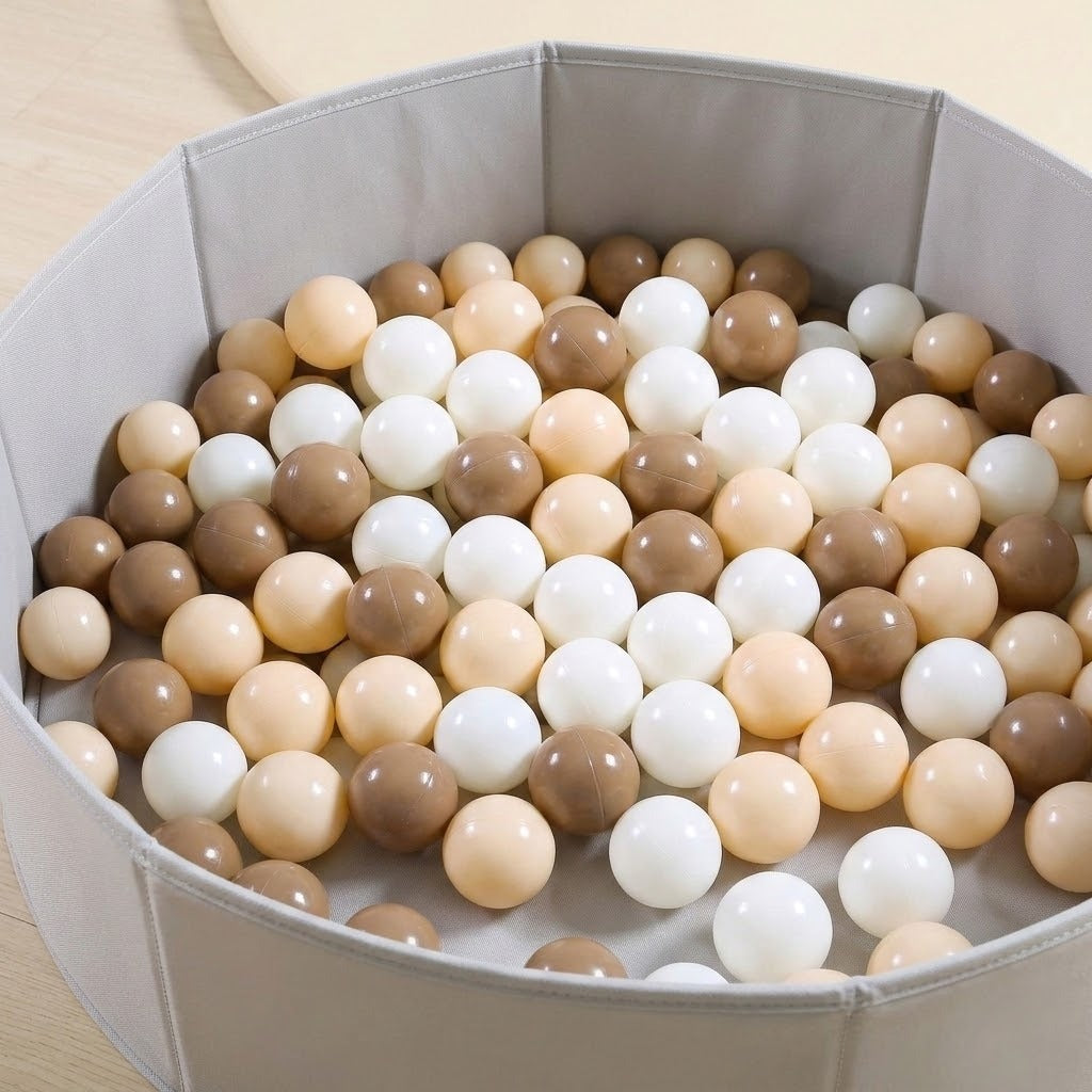 A round gray fabric ball pit filled with smooth plastic balls in neutral shades of beige, cream, white, and light brown.