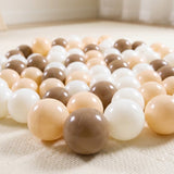 Glossy plastic ball pit balls in mocha brown, cream, and white lie scattered across a light textured rug.