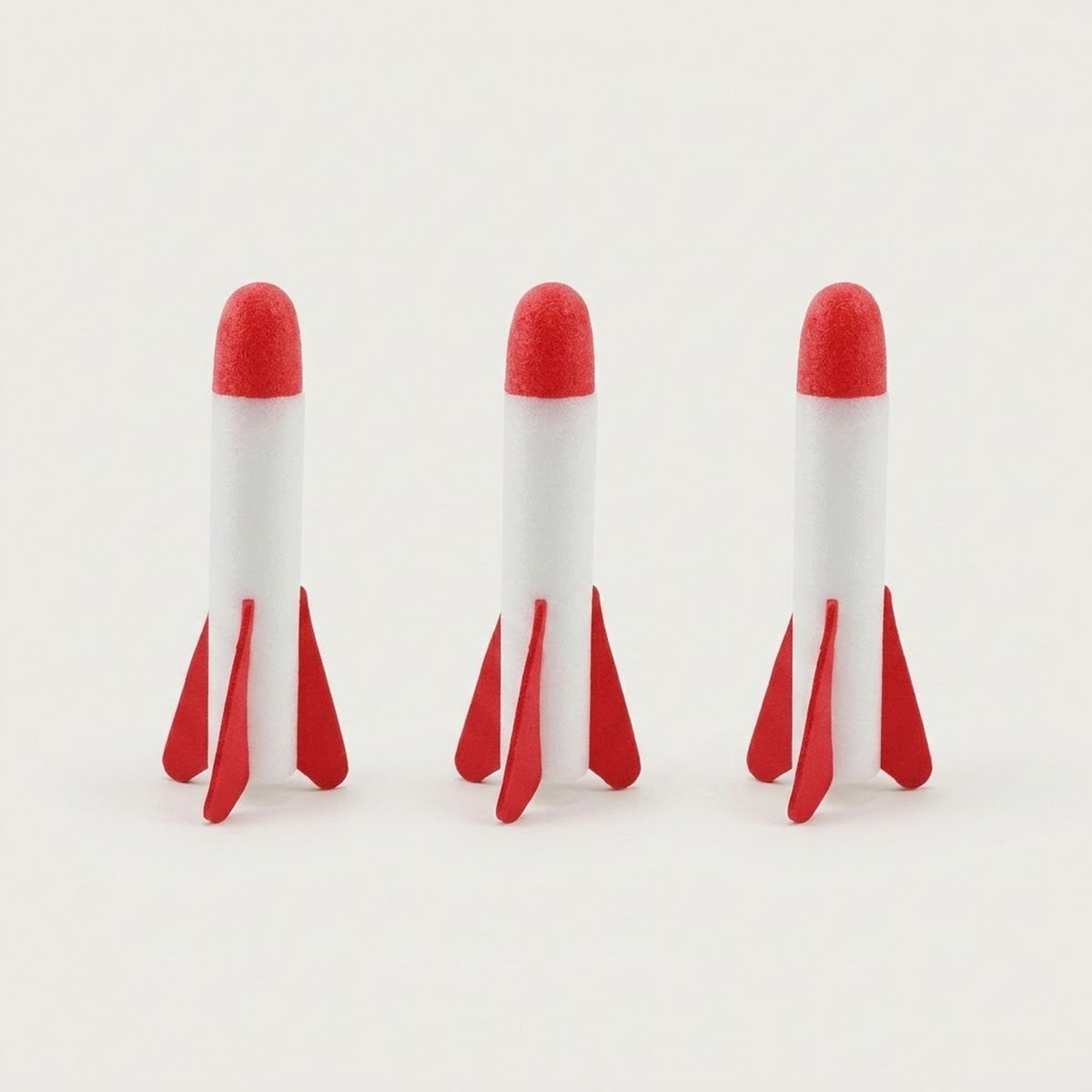 Three foam rockets for the rocket launcher stand in a row, with white bodies, red tips and fins against a light background.