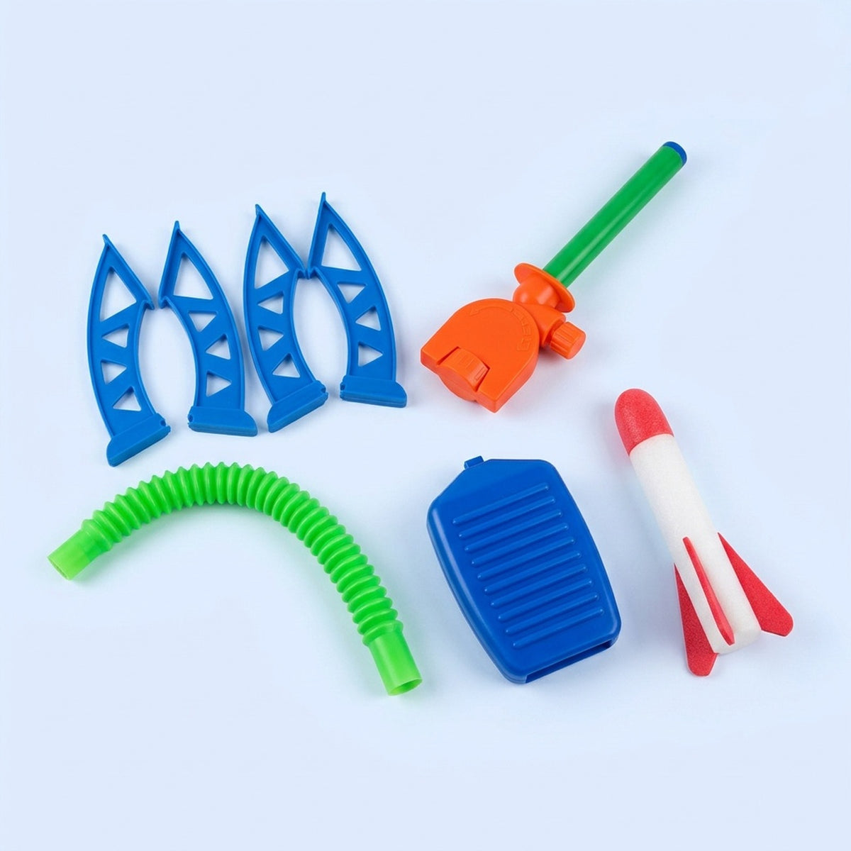 A set of colorful plastic toy parts laid out on a light blue background, including four blue wing-like pieces, a green flexible tube, an orange and green launcher, a blue rectangular piece, and a red-and-white rocket.
