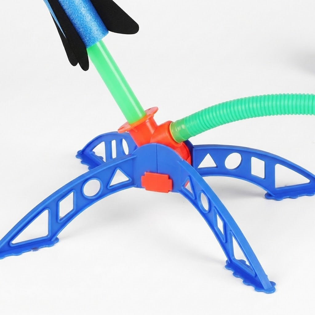 A colorful plastic toy rocket launcher with a blue four-legged base, an orange center, and green flexible tubes, shown on a white background with a partially visible blue and black rocket.