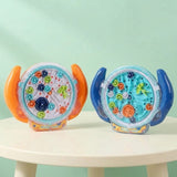 Two round transparent plastic maze puzzle variants with orange and blue handles stand on a white table against a pale mint background.