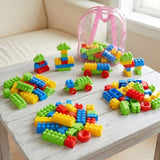 Colorful children's building blocks scattered on a light wooden table, with a clear pink backpack filled with more blocks in the background near a window.