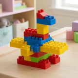 Large red, yellow, blue and green ABS plastic building blocks assembled into a bird on a light wooden table in a softly blurred playroom.
