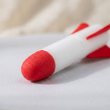 A foam rocket for the rocket launcher rests on a pale surface, showing its textured red nose, white body, and red fins.