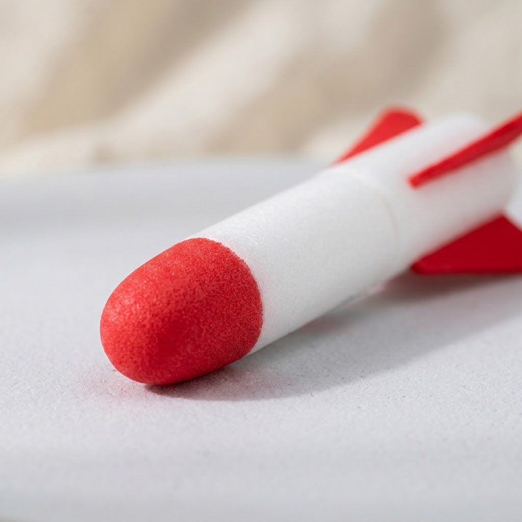 A foam rocket for the rocket launcher rests on a pale surface, showing its textured red nose, white body, and red fins.
