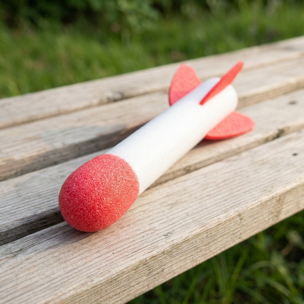 A red-and-white foam rocket for the rocket launcher rests on a wooden bench against a blurred green garden background.