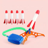 Rocket launcher with an orange base, blue pedal, green hose, and five red-and-white foam rockets sits against a pale pink background.