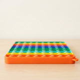 Rainbow silicone counting toy lies flat on a light wooden surface, showing numbered bubbles and an orange rim against a cream background.