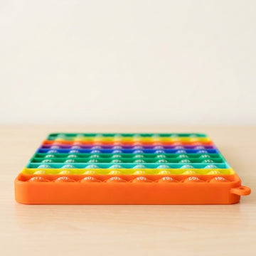 Rainbow silicone counting toy lies flat on a light wooden surface, showing numbered bubbles and an orange rim against a cream background.