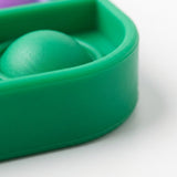 Close-up shows the counting toy’s green silicone bubble and thick rounded corner rim resting on a white surface.