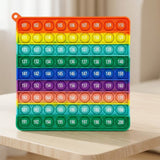 Rainbow silicone counting toy stands on a light wooden tabletop, displaying numbered bubbles against a softly blurred beige indoor background.