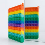 Rainbow silicone counting toy stands upright beside a mirror, showing colorful bubble rows and a corner loop against a pale background.